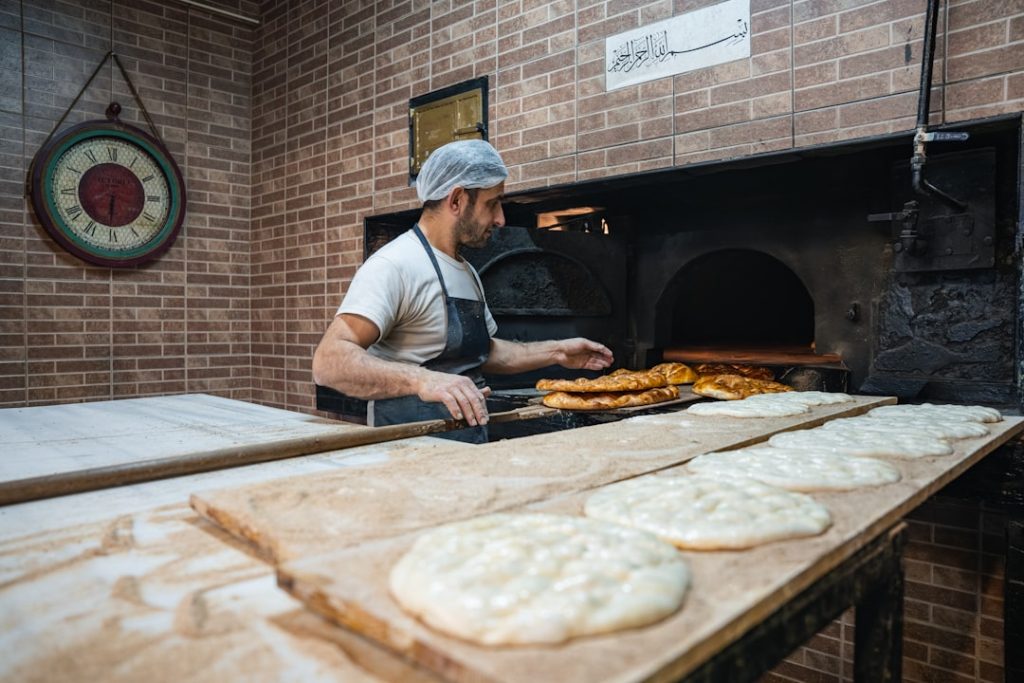 A master baker placing the first batch of Ramadan pide into the traditional stone oven, marking the start of the daily iftar preparation.