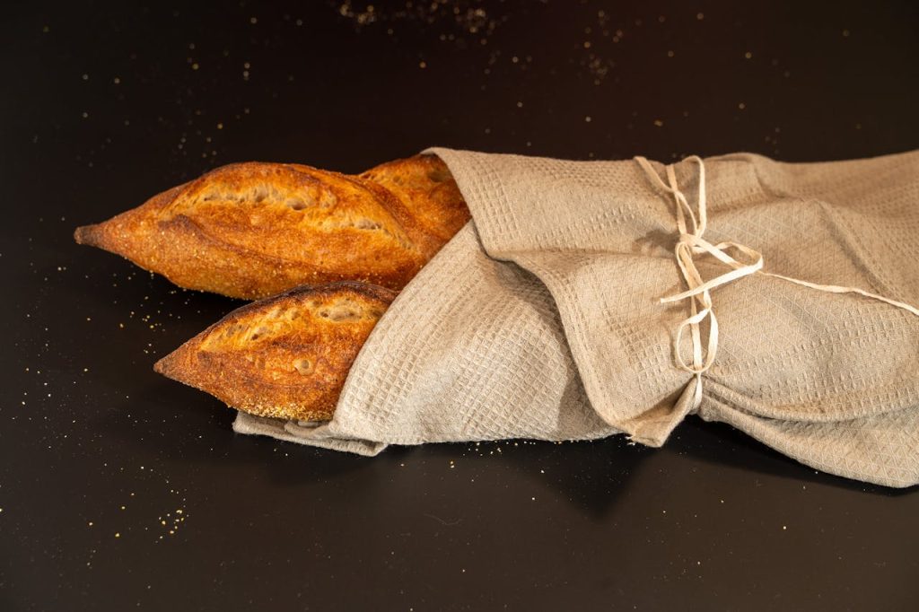 Two freshly baked artisan baguettes wrapped in a linen cloth on a dark surface.
